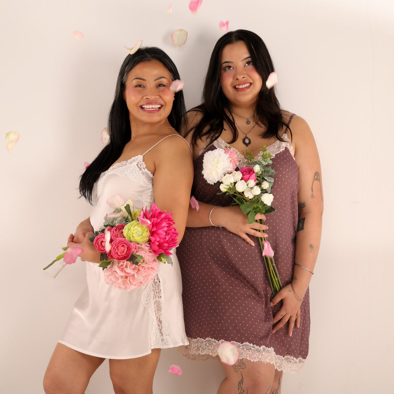 Two women holding flower bouquets against a plain background